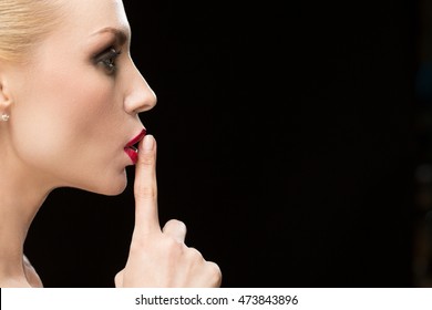 Our Little Secret. Closeup Portrait Of A Profile Of A Stunning Beautiful Red Lipped Woman Shushing With Her Finger To Her Lips On Black Background Copyspace On The Side 