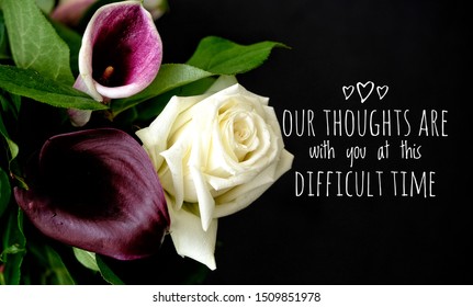 Our thoughts are with you at this difficult time. Words with purple and white flowers on black background. Sympathy or condolence card