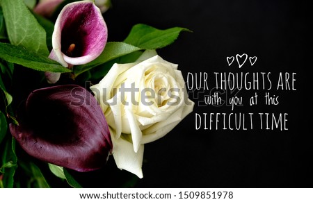 Our thoughts are with you at this difficult time. Words with purple and white flowers on black background. Sympathy or condolence card