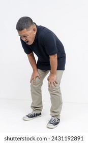 Out of breath middle aged Asian man showing signs of exhaustion, leaning on his knees. Lacking fitness. Isolated on a white background.