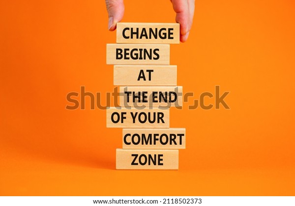 Out from comfort zone symbol. Wooden blocks with\
words Change begins at the end of your comfort zone. Beautiful\
orange background, copy space. Businessman hand. Business out from\
comfort zone concept.