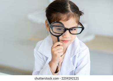 Out of curiosity, a cute young girl is playing with a magnifying glass as a mischievous childhood toy in the school lab. Concept education, Science experiments, Chemistry - Powered by Shutterstock