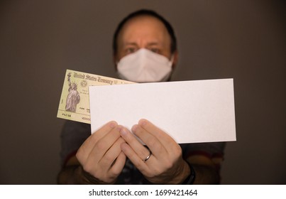 Out of focus caucasian man wearing face mask or N95 respirator holding a United States Treasury check representing economic impact payment as part of stimulus package due to  the COVID-19 coronavirus.