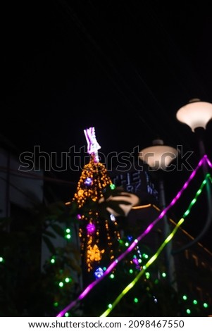 Out of focus chirstmas tree with star on top decorated with lights and street lamp with colorful lights hanging. Background. Lens Flare.