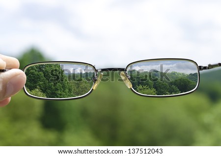 out of focus nature with hand holding a glasses that correct the vision