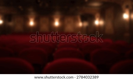An out of focus perspective of rows of empty red velvet chairs inside a dark theater hall with glowing wall lights