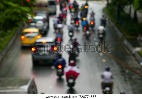 Out of focus. Undefined poeple ride motorcycle with\
raincoat in rain. 