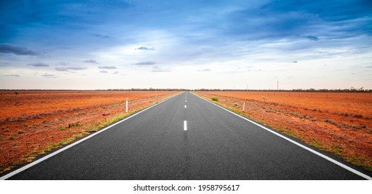 Outback Queensland Road In Australia With A Stormy Sky. An Empty Open Road Stretching To The Horizon. Single Lane Sealed Highway With Deep Orange Red Soil On Both Sides. Travel Adventure.