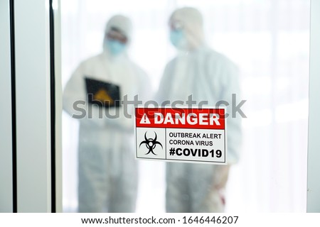 Outbreak alert Coronavirus COVID 19, COVID 19 signage in front of control area with doctors in personal protective equipment inside.