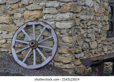 An Outdated Old Wooden Wheel From A Horse-drawn Cart Near The Stone Wall Of An Ancient House. Detail Of A Wooden Old Carriage. Rural Retro Still Life. Decorations In The Yard. Place For Text. Ukraine.