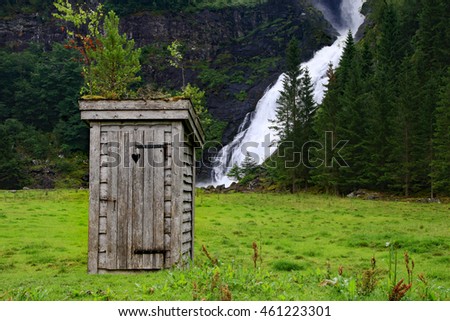 Outdated outdoor privy in front of a foaming waterfall