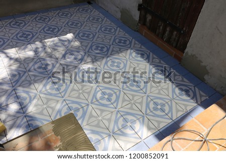Outddor view of a man laying square ceramic tiles on a terrace floor. Geometric alignment of blue and white elements. Renovation of an ancient exterior place.