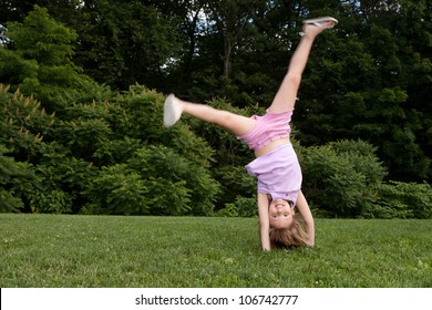 Outdoor Action Shot Of A Little Girl In Pink Doing A Cartwheel With Motion In Her Legs