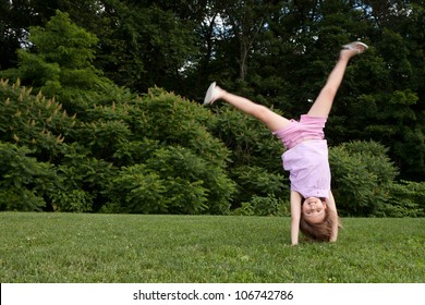 Outdoor action shot of a little girl in pink doing a cartwheel with motion in her legs