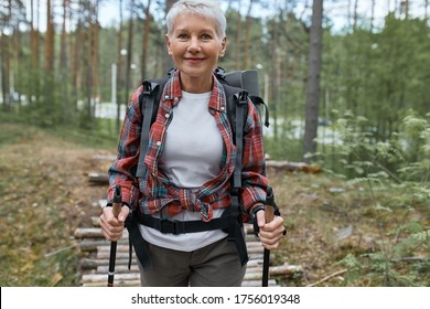 Outdoor Activities, People And Vacations Concept. Attractive Short Haired Middle Aged Woman In Activewear Hiking In Forest Using Poles For Nordic Walking, Doing Aerobic Workout, Enjoying Nature