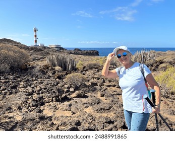 Outdoor activity in nature for a carefree sporty senior woman walking along a rocky beach in direction to a lighthouse enjoying healthy lifestyle and freedom in good sunny day with blue sky - Powered by Shutterstock