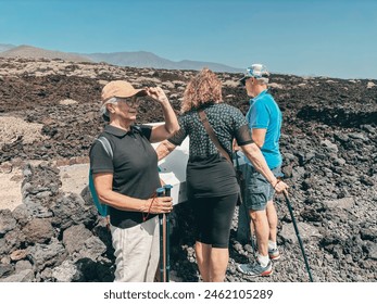 Outdoor activity in nature concept. Group of sporty mature friends enjoying healthy lifestyle hiking along a rocky beach in southern Tenerife stops to read touristic informations. - Powered by Shutterstock