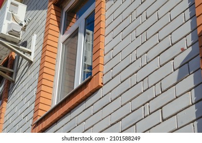 Outdoor Air Conditioner Unit Against A White Brick Wall. A Window Framed In Red Brick. Daytime. Selective Focus. No People.