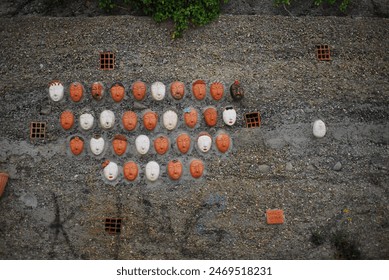 An outdoor art installation featuring white and red masks arranged on a gravel surface, Italy