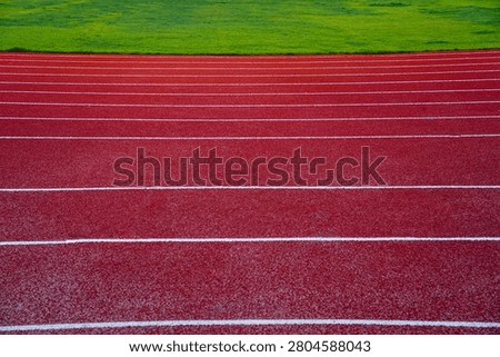 An outdoor athletic running track with multiple white lane markings, adjacent to a green grass field, suitable for sports and competitions.