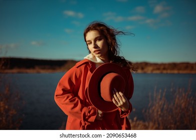 Outdoor Autumn Fashion, Lifestyle Portrait Of Elegant Woman Wearing Trendy Orange Trench Coat, Holding Classic Hat, Posing In Nature. Copy, Empty Space For Text