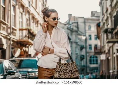 Outdoor Autumn Fashion Portrait Of Elegant, Luxury Lady Wearing Sunglasses, Trendy White Shirt, Wrist Watch, Holding Animal, Leopard Print Bag, Posing In Street Of European City. Copy, Empty Space