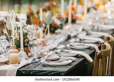 Outdoor banquet and modern design for boho wedding ceremony in summer. Linen tablecloth, candles, flowers and accessories, glasses and plates on wooden table for guests with chairs, flat lay, nobody