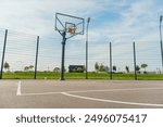 Outdoor basketball court with a metal hoop and fencing, captured under a vibrant, clear blue sky.

