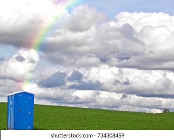 outdoor blue portable toilet with rainbow on rural green hill and sky horizon