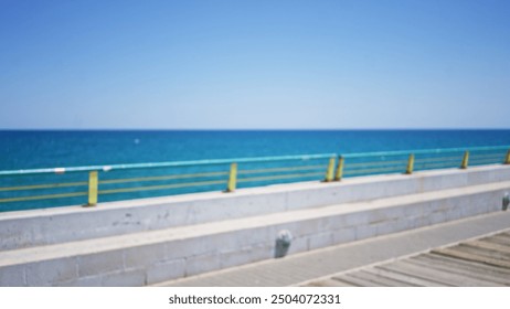 Outdoor blurred image of a seaside pier with turquoise handrails and a clear blue ocean horizon under a bright blue sky. - Powered by Shutterstock