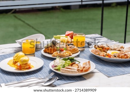 Outdoor breakfast setting with eggs Benedict, croissants, fresh juice, and fruit on table. Perfect for dining, brunch, or hotel ad.