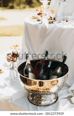 Outdoor buffet setup featuring a silver ice bucket holding sparkling wine and champagne bottles, with desserts in background