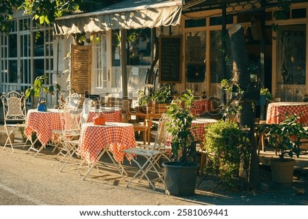 outdoor cafe with cute small tables in the warm sunlight. cosy street and European style restaurant with flowers in the pots and red tablecloth tables