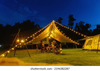 Outdoor camping tent with tarp or flysheet on grass courtyard and warm night light under dark blue sky twilight time, family vacation picnic on holiday relax, Overview of camping of family tourist. - Shutterstock ID 2196382287