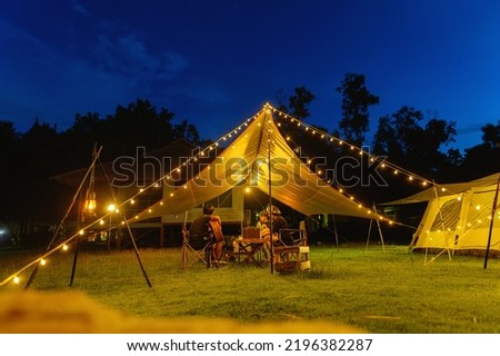 Outdoor camping tent with tarp or flysheet on grass courtyard and warm night light under dark blue sky twilight time, family vacation picnic on holiday relax, Overview of camping of family tourist.