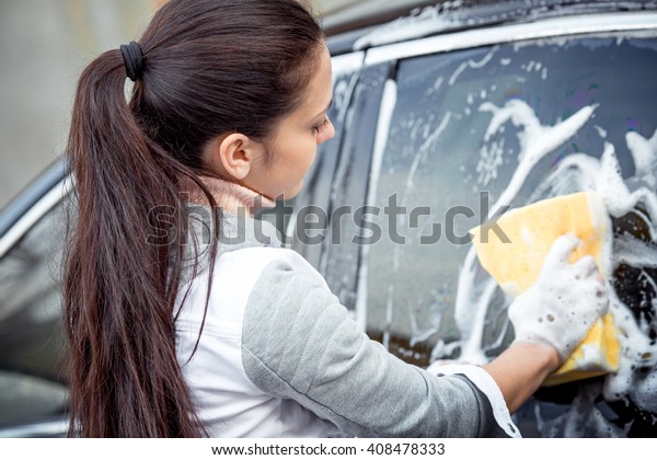 outdoor car wash with yellow sponge. Beautiful girl\
washes the car