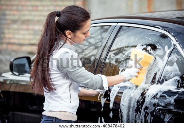 outdoor car wash with yellow sponge. Beautiful girl\
washes the car