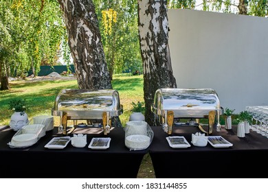 Outdoor catering banquet in summer. Banquet table with chafing dish, plates and cutlery