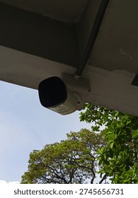 Outdoor CCTV security camera installed under building roof. Surveillance and safety monitoring concept in urban area.