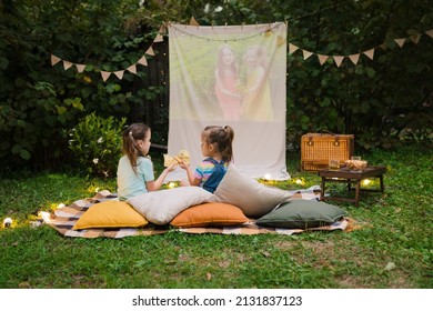 Outdoor cinema theater Backyard Family outdoor movie night with kids. Sisters spending time together, watching cimema at backyard DIY Screen with film. Summer outdoor weekend activities with children