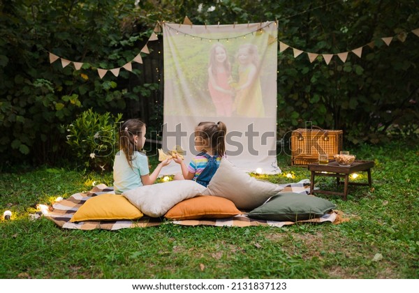 Outdoor cinema theater Backyard Family outdoor\
movie night with kids. Sisters spending time together, watching\
cimema at backyard DIY Screen with film. Summer outdoor weekend\
activities with\
children