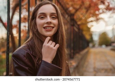 Outdoor close up autumn portrait of young elegant happy smiling woman wearing trendy faux leather trench coat, posing in street. Copy, empty space for text