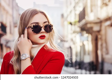 Outdoor close up fashion portrait of young beautiful fashionable woman wearing stylish turtle frame sunglasses, luxury wrist watch, red blazer, posing in street of european city. Copy, empty space
 - Powered by Shutterstock
