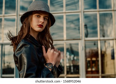 Outdoor Close Up Fashion Portrait Of Young Elegant Model, Woman Wearing Trendy Bucket Hat, Black Wrist Watch, Leather Coat, Posing In Street Of City. Copy, Empty Space For Text