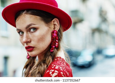 Outdoor Close Up Portrait Of Young Beautiful Fashionable Confident Woman With Freckles, Red Lips Makeup, Wearing Total Red Look: Hat, Floral Sequin Earrings, Dress. Model Posing In Street. Copy Space