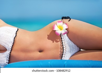 outdoor close up shot of young woman in white bikini, sunbathing at sea beach
