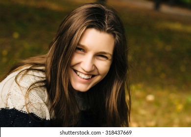 Outdoor closeup colorful autumn portrait of young natural happy laughing girl with natural smile in warm sweater in park