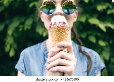 Outdoor closeup fashion portrait of young hipster crazy girl eating ice cream in summer hot weather in round mirror sunglasses have fun and good mood. Toned style instagram filters