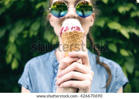 Outdoor closeup fashion portrait of young hipster crazy girl eating ice cream in summer hot weather in round mirror sunglasses have fun and good mood. Toned style instagram filters