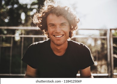Outdoor closeup portrait of handsome freckled smiling male with curly hair, posing for social advertisement, in the city street on sunset sunlight with copy space for your promotional information